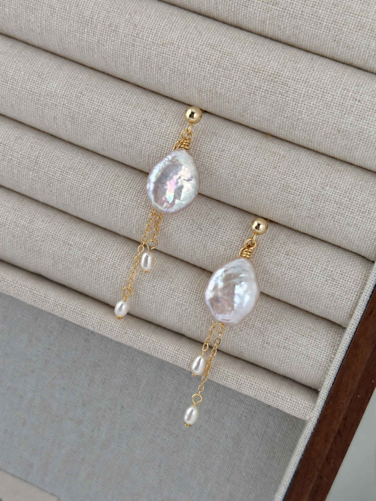 Close view of Lilt baroque pearl earrings on a linen jewelry tray, showing iridescent pearls and fine gold chains.
