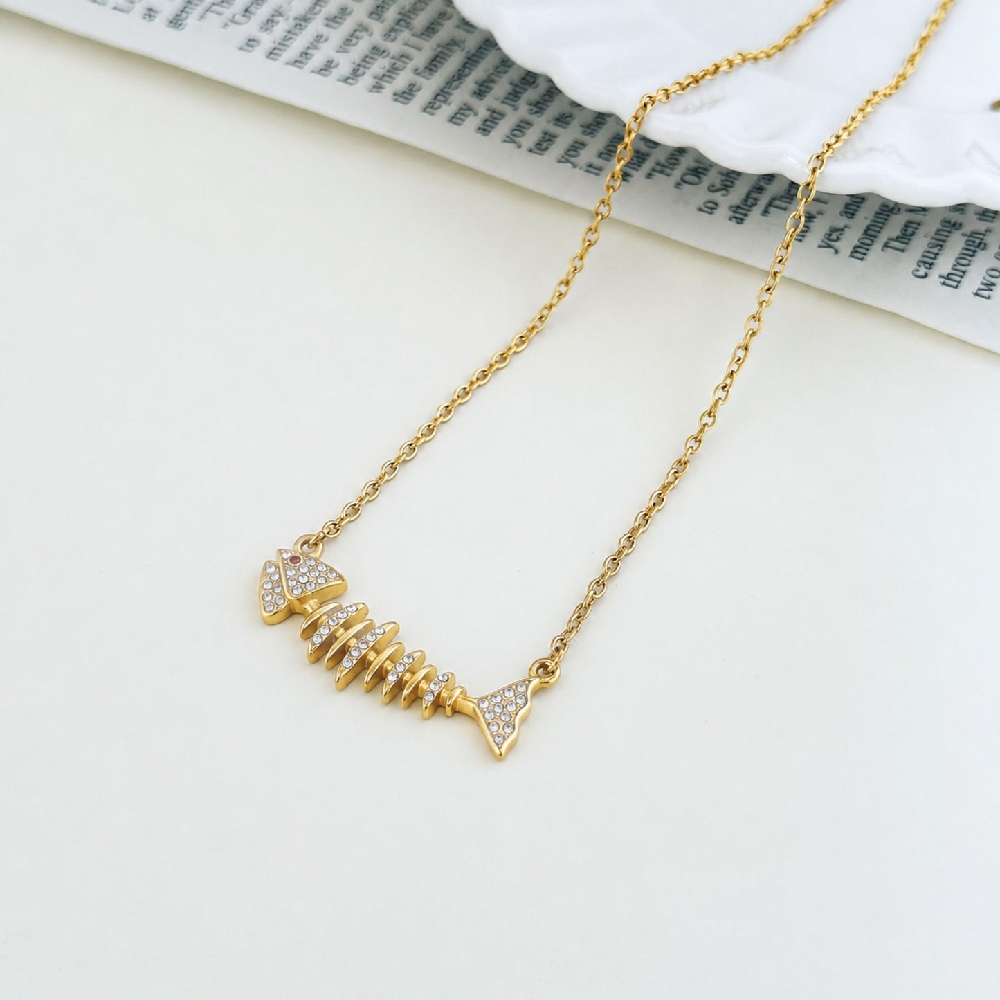 Gold fishbone necklace styled on a soft neutral surface with coastal details.