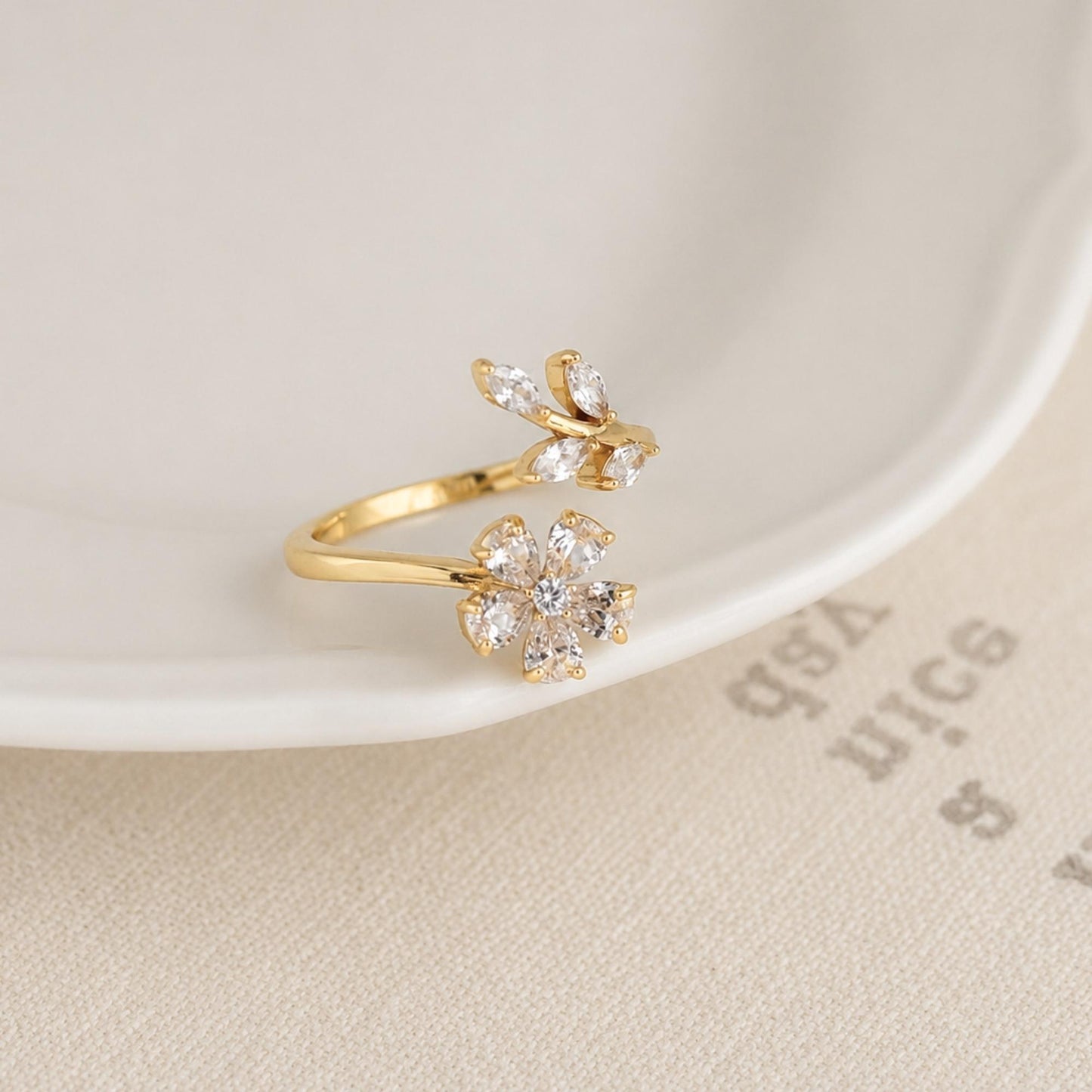 Gold zircon flower ring photographed on a soft neutral surface.