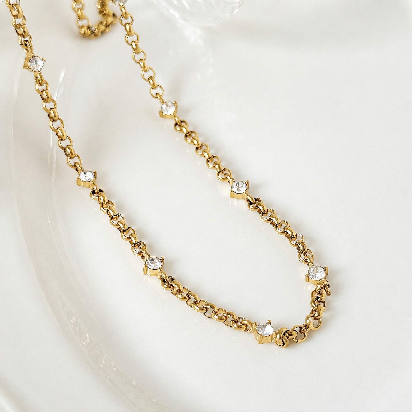 Gold zircon chain necklace arranged on clear glass in natural light.