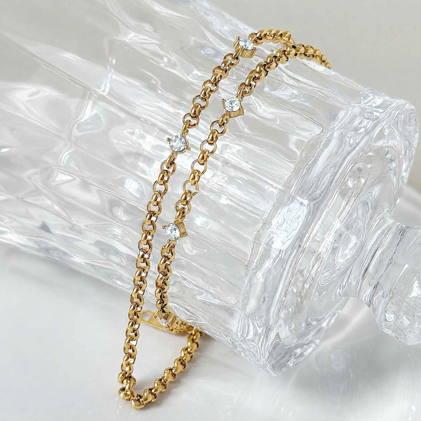 Close-up of gold chain links with small zircon stones in soft natural light.