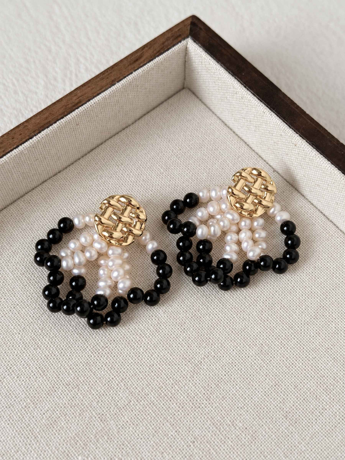Loom pearl and black agate earrings arranged on a neutral linen jewelry tray.