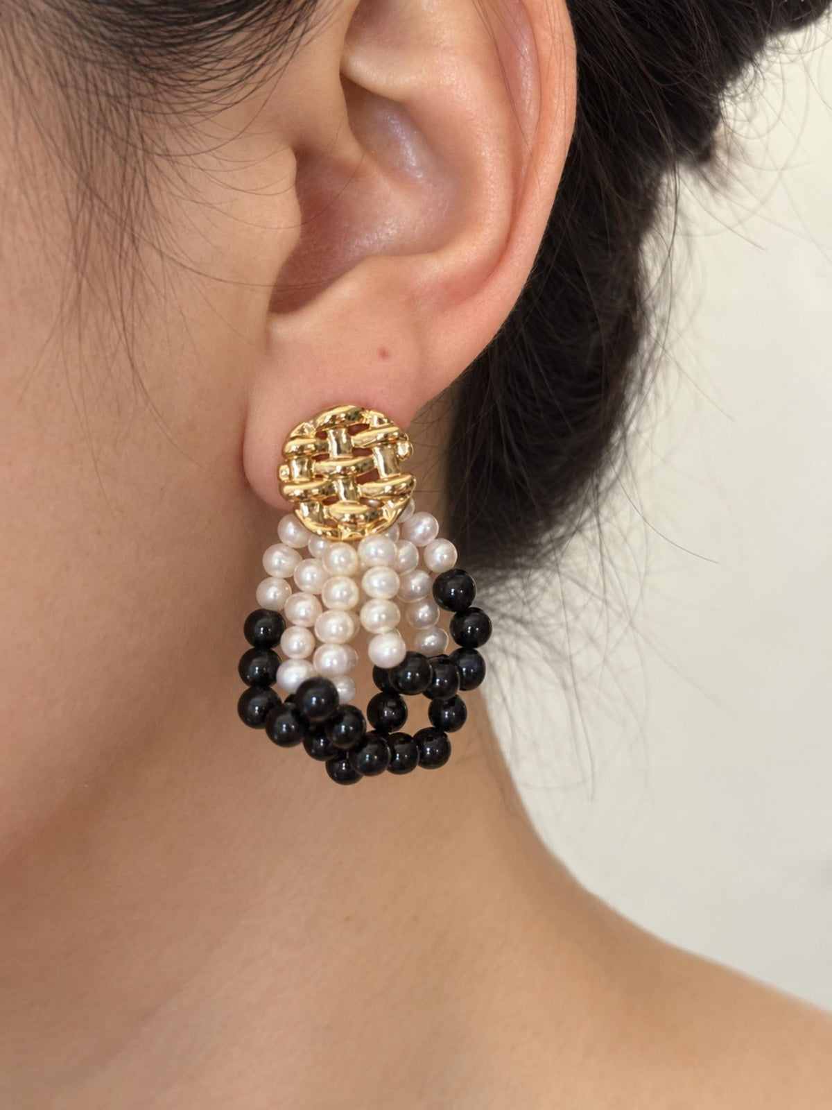 Loom black agate and freshwater pearl earrings worn in side profile with a sculptural gold-tone stud.