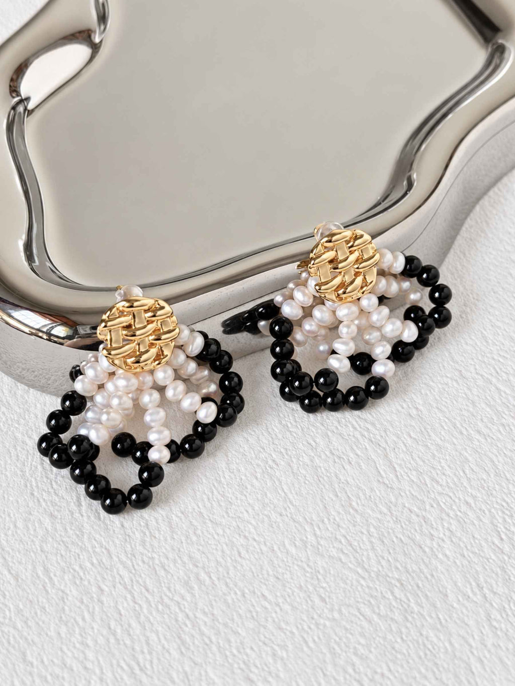 Loom black agate and freshwater pearl earrings styled beside a reflective silver tray.