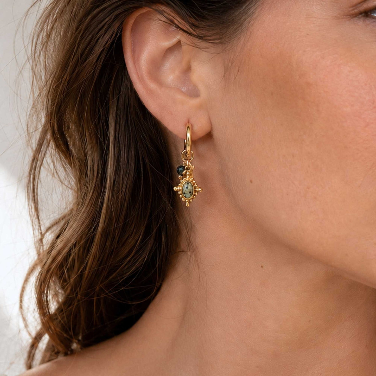 Gold natural stone charm hoop earrings worn in warm coastal light