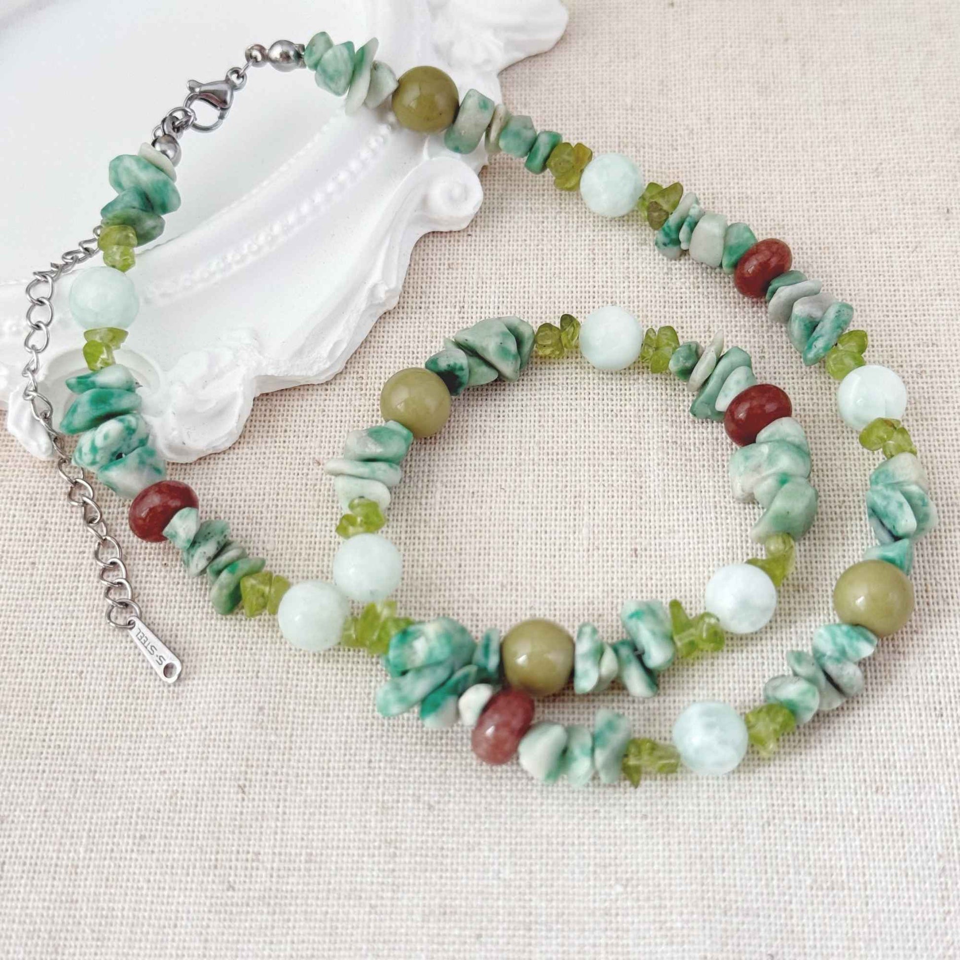 Close-up of green apatite, mixed natural stone beads, olive tones, and stainless steel clasp.