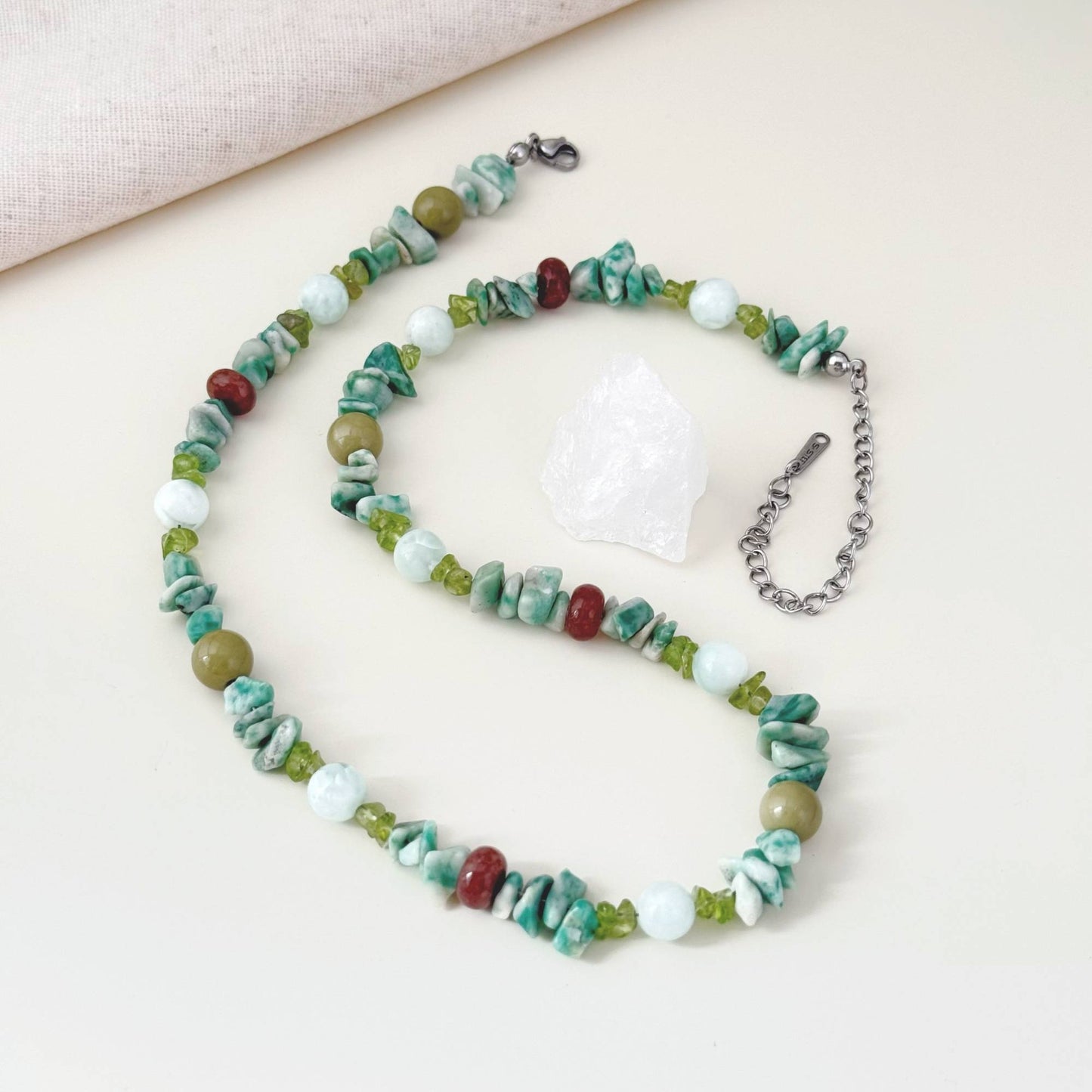 Green mixed stone necklace arranged on linen with soft natural light.
