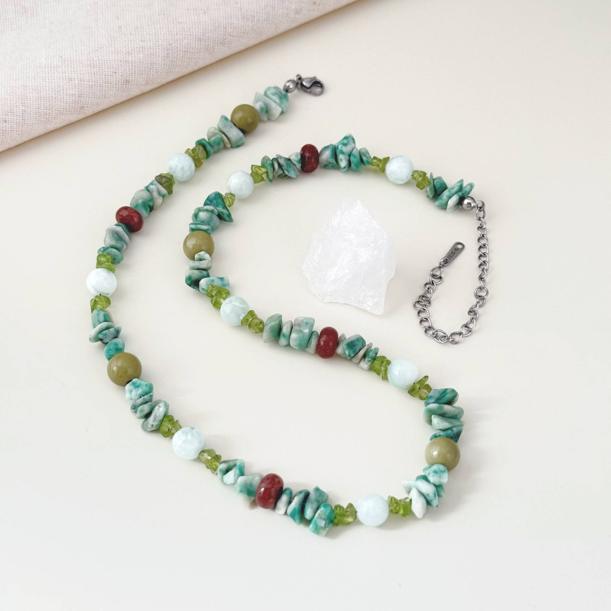 Green mixed stone necklace arranged on linen with soft natural light.