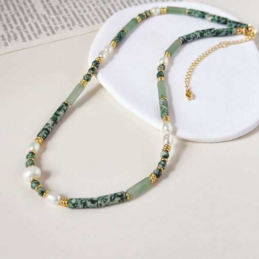 Soft green natural stone and pearl necklace styled on a white surface with warm gold hardware.