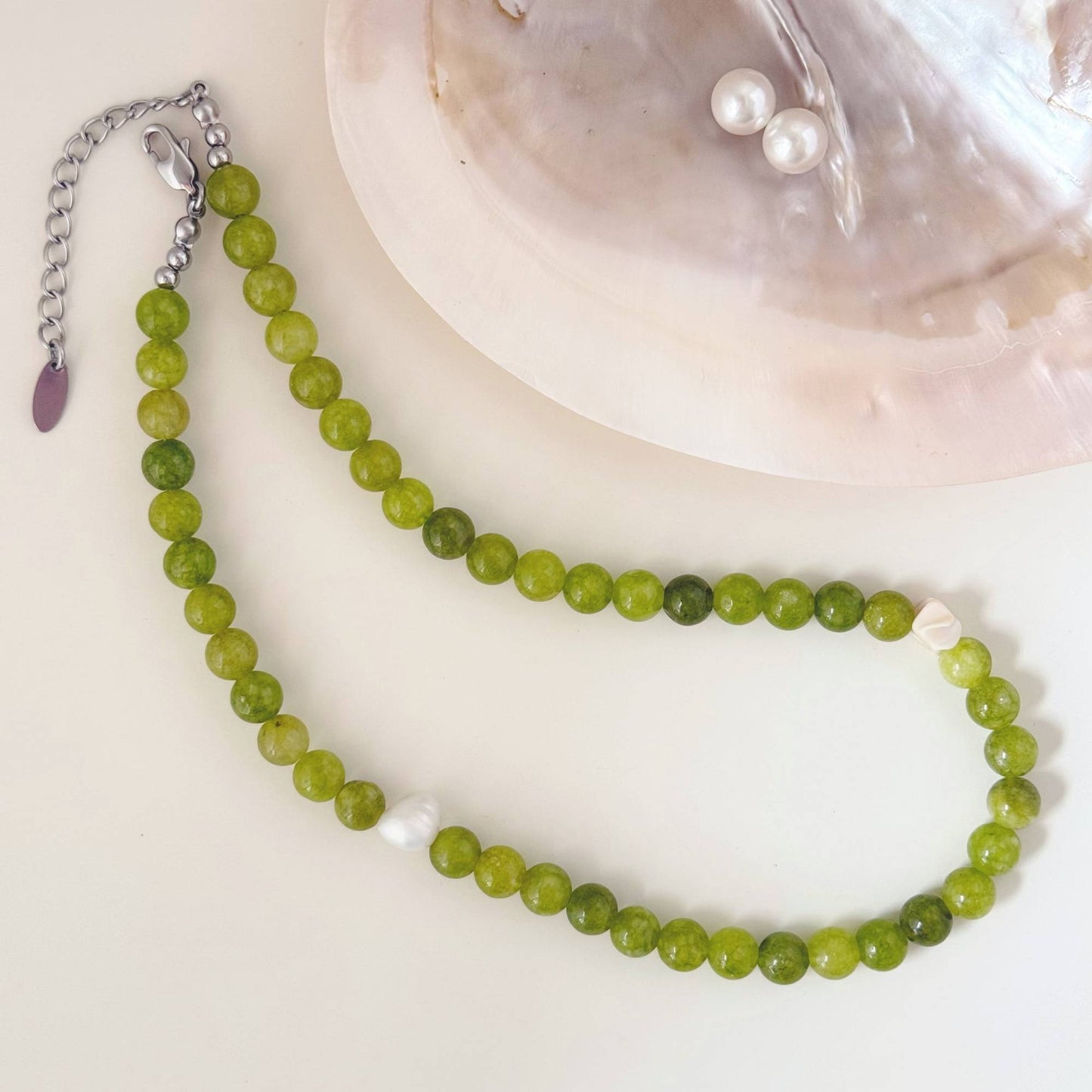 Close-up of olive green stone beads, freshwater pearl, shell accents, and stainless steel hardware.