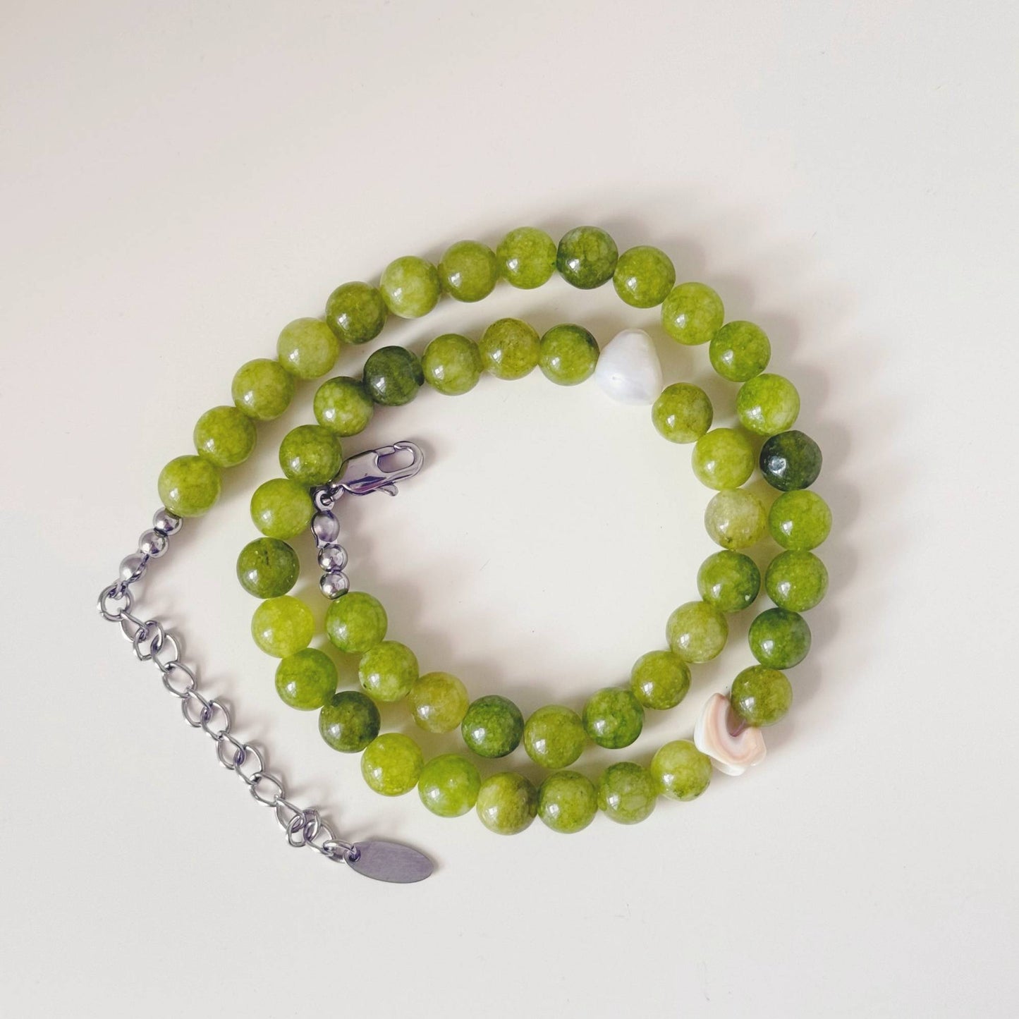 Green stone and pearl necklace styled beside a shell in soft natural light.