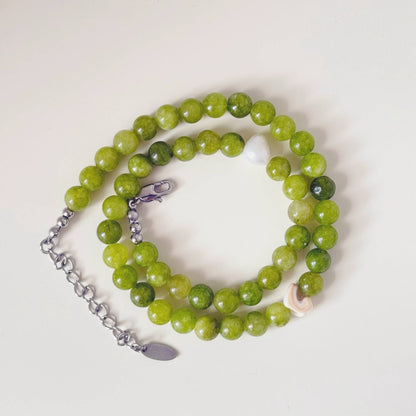 Green stone and pearl necklace styled beside a shell in soft natural light.