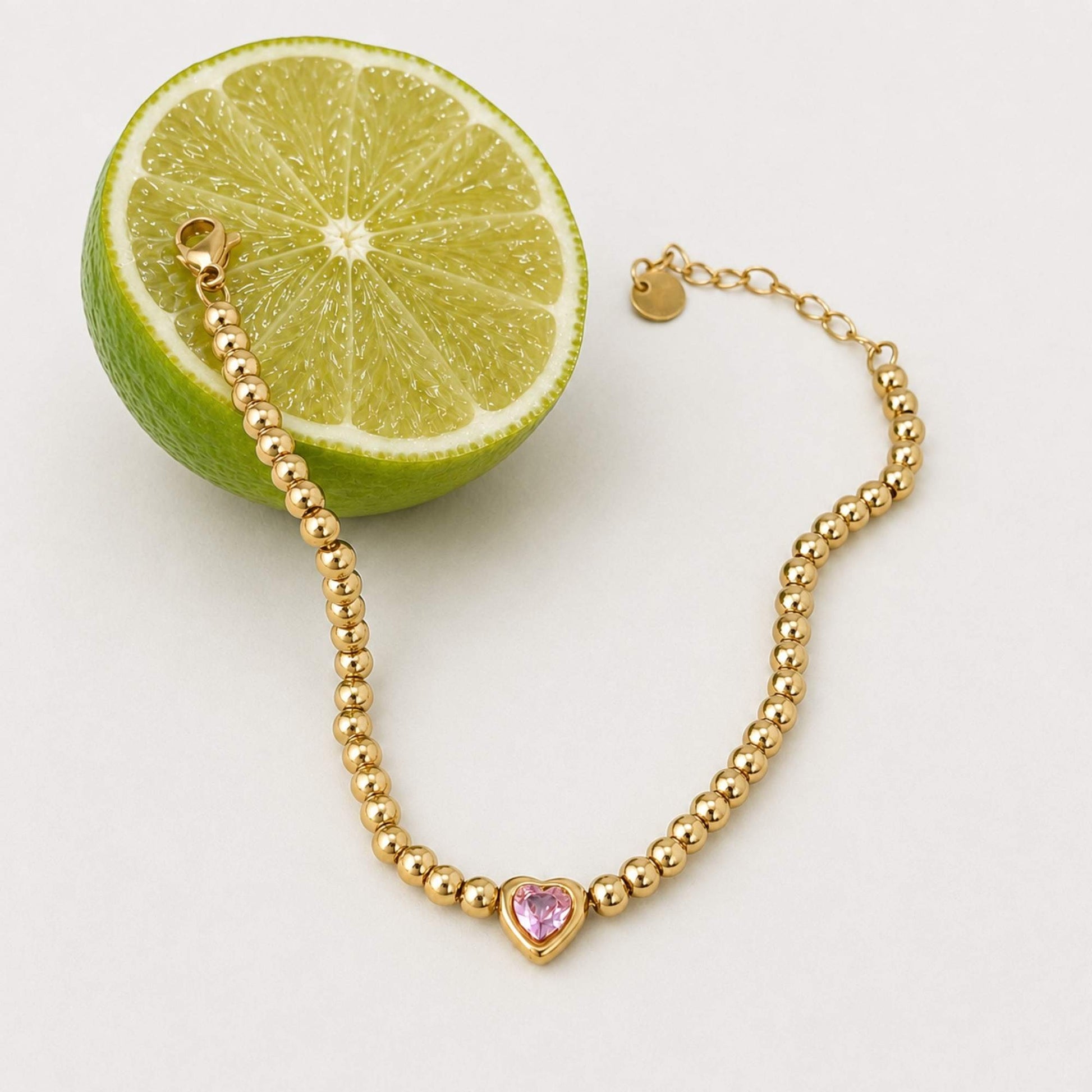 Gold bead and pink heart bracelet styled beside a fresh lime on a light surface