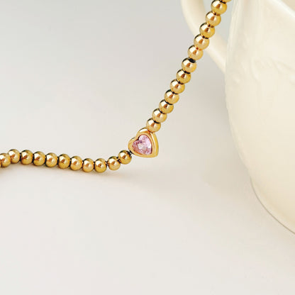 Close-up of the pink cubic zirconia heart centerpiece and polished gold beads on the One Heart Bracelet