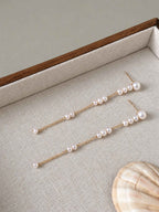 Long freshwater pearl earrings arranged on a linen jewelry tray beside a natural shell.