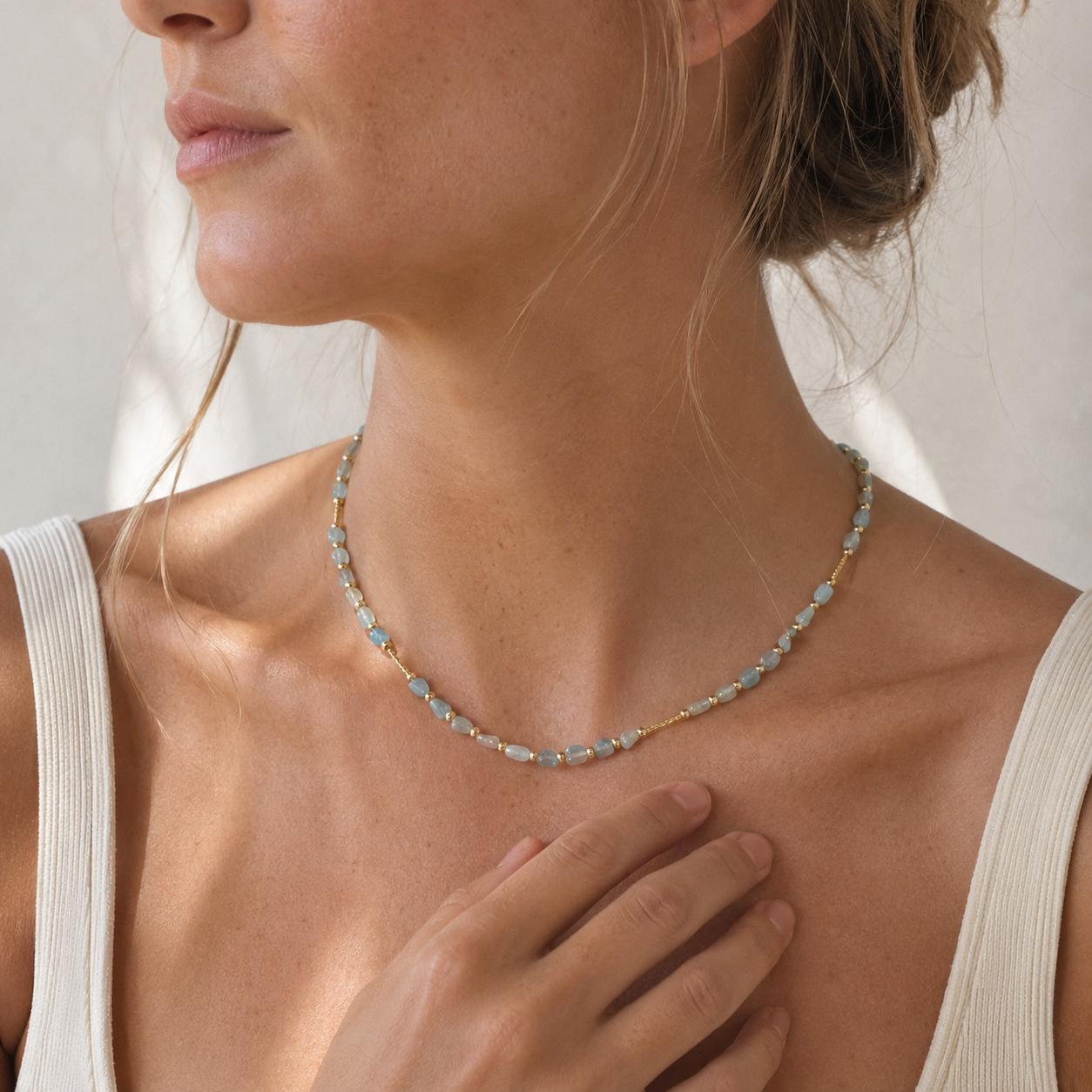 Model wearing a delicate pale blue stone necklace with a white tank in warm natural light.