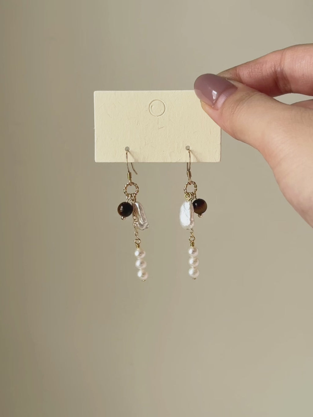 Six-second video transitioning from the full pair on a display card to a worn close-up, highlighting the contrast between tiger’s eye, freshwater pearls and natural movement.