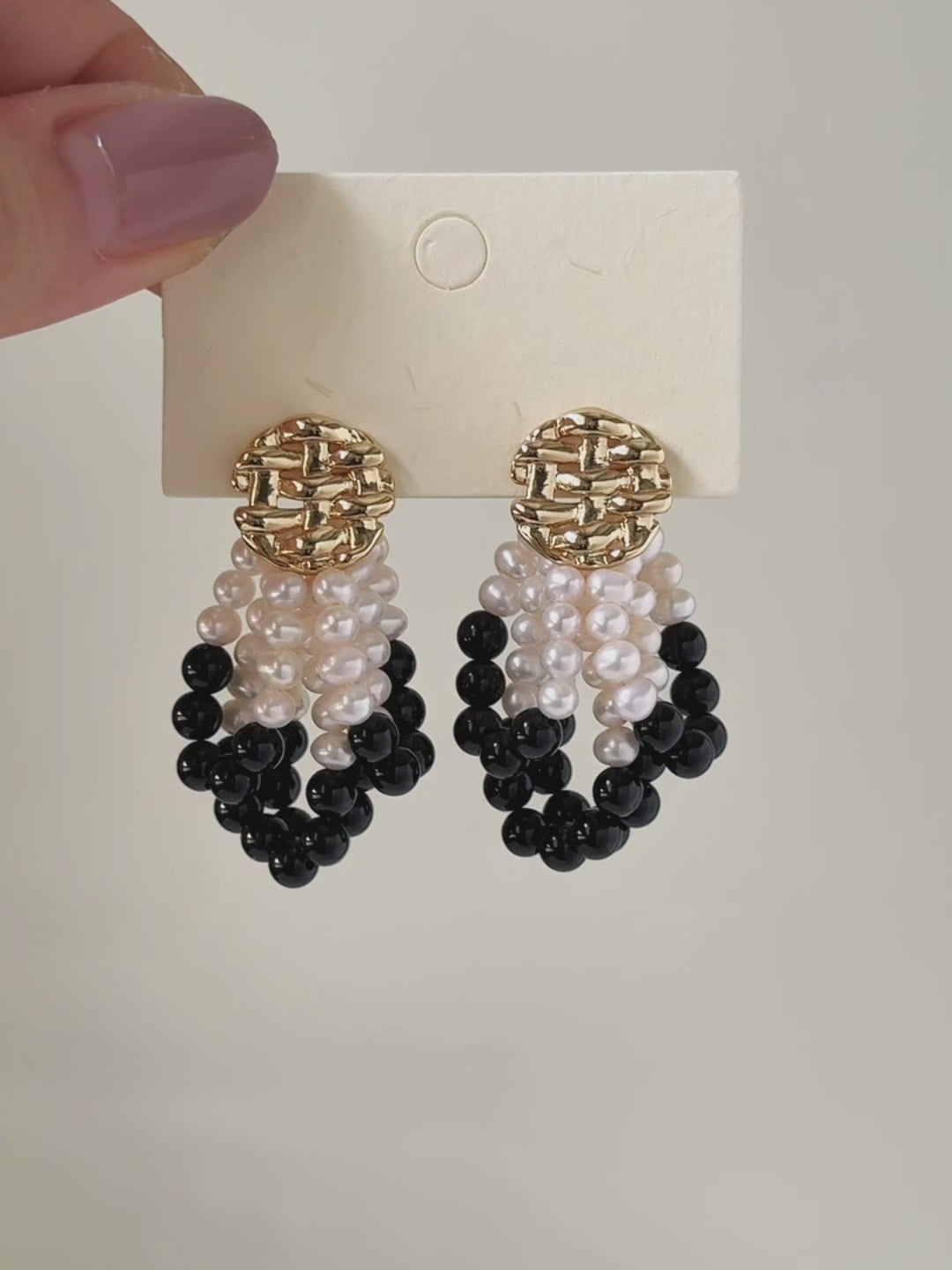 Six-second product video transitioning from the full pair on a display card to a worn close-up, showing the layered pearl and black agate loops in motion.