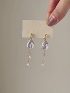 Six-second product video showing the Lilt earrings on a display card before transitioning to a close-up worn view, highlighting the iridescent baroque pearls and natural chain movement.