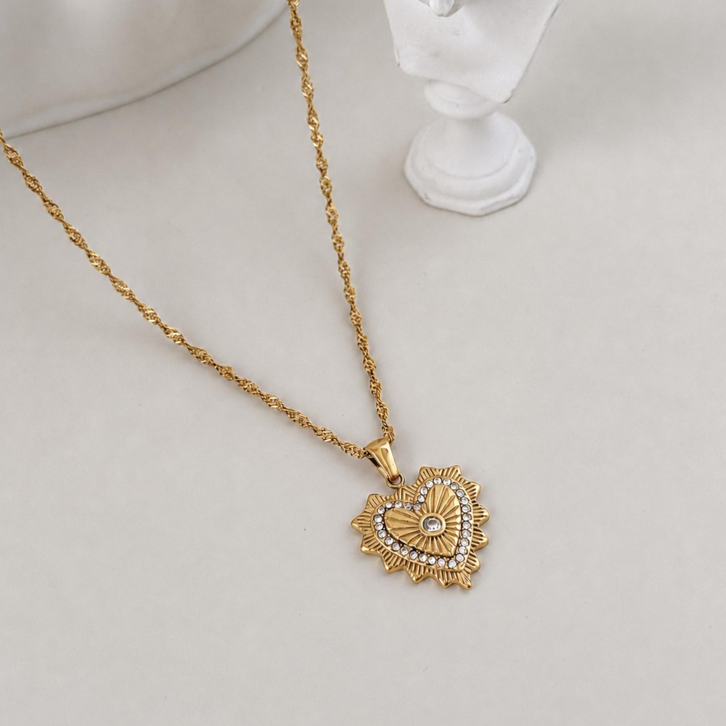Gold Radiant Heart Pendant Necklace styled beside a white sculptural bust on a soft ivory surface