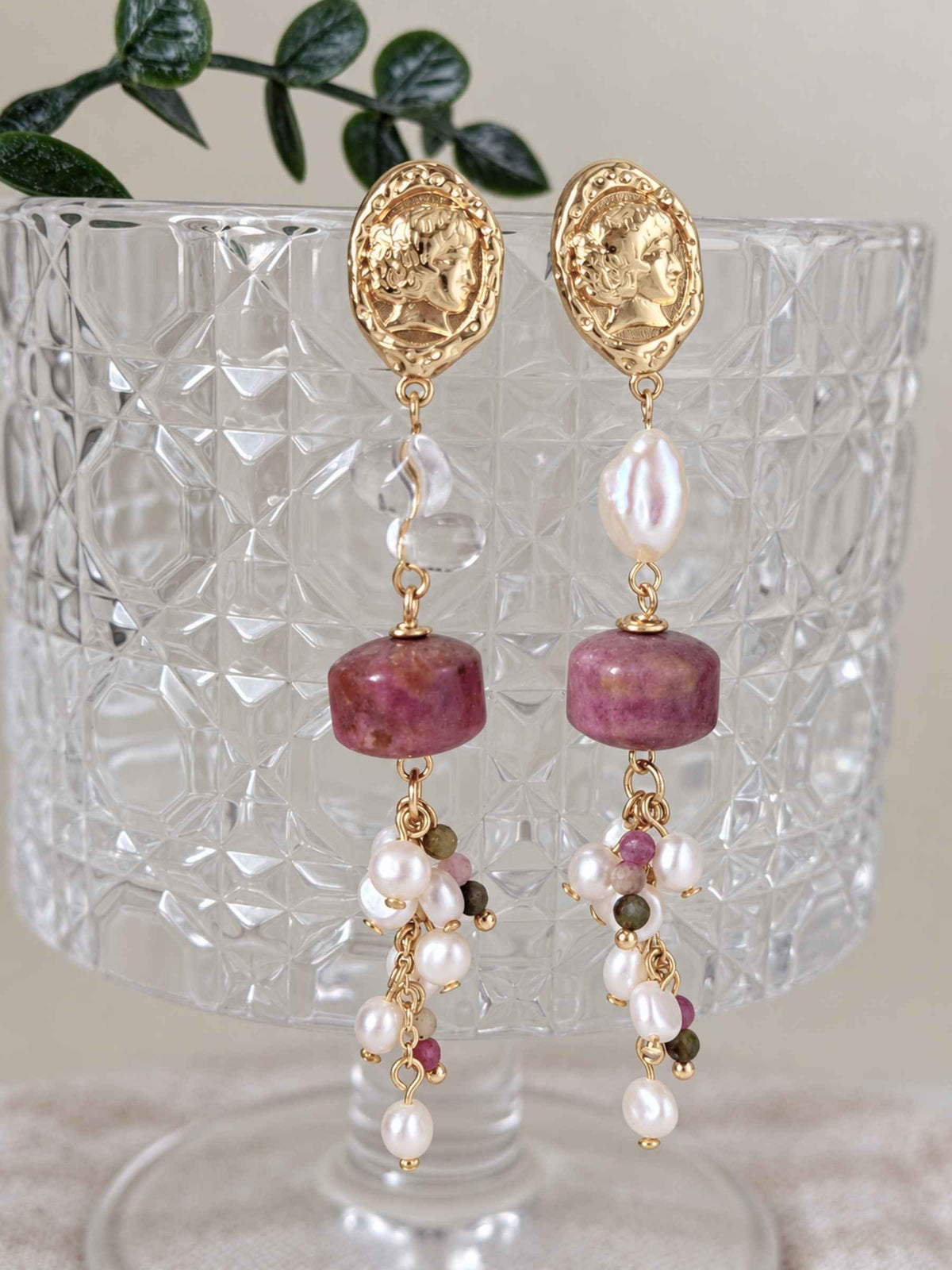 Relic rhodonite and pearl earrings displayed against textured clear glass with clustered gemstone drops.