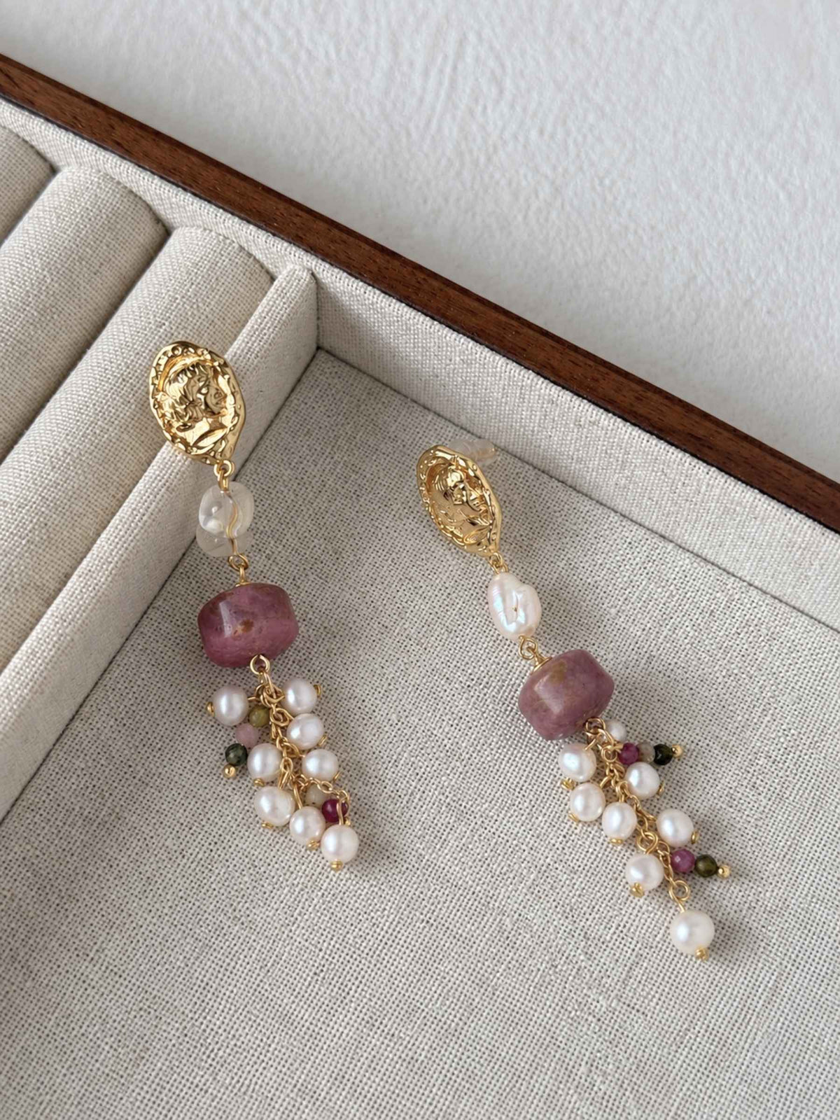 Relic rhodonite and freshwater pearl earrings arranged on a neutral linen jewelry tray.