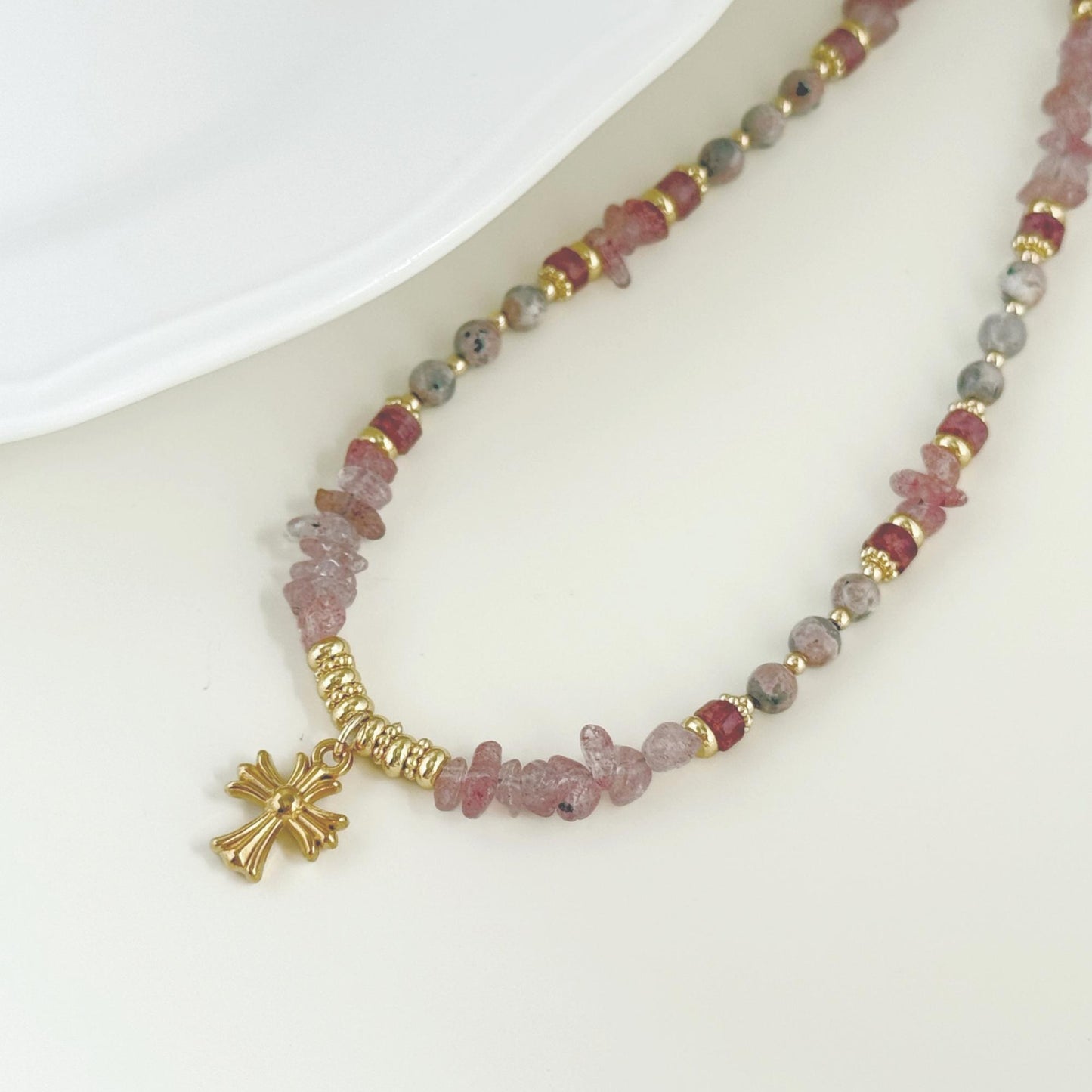 Close-up of pink strawberry quartz beads, mixed natural stone accents, and a small gold-tone charm.