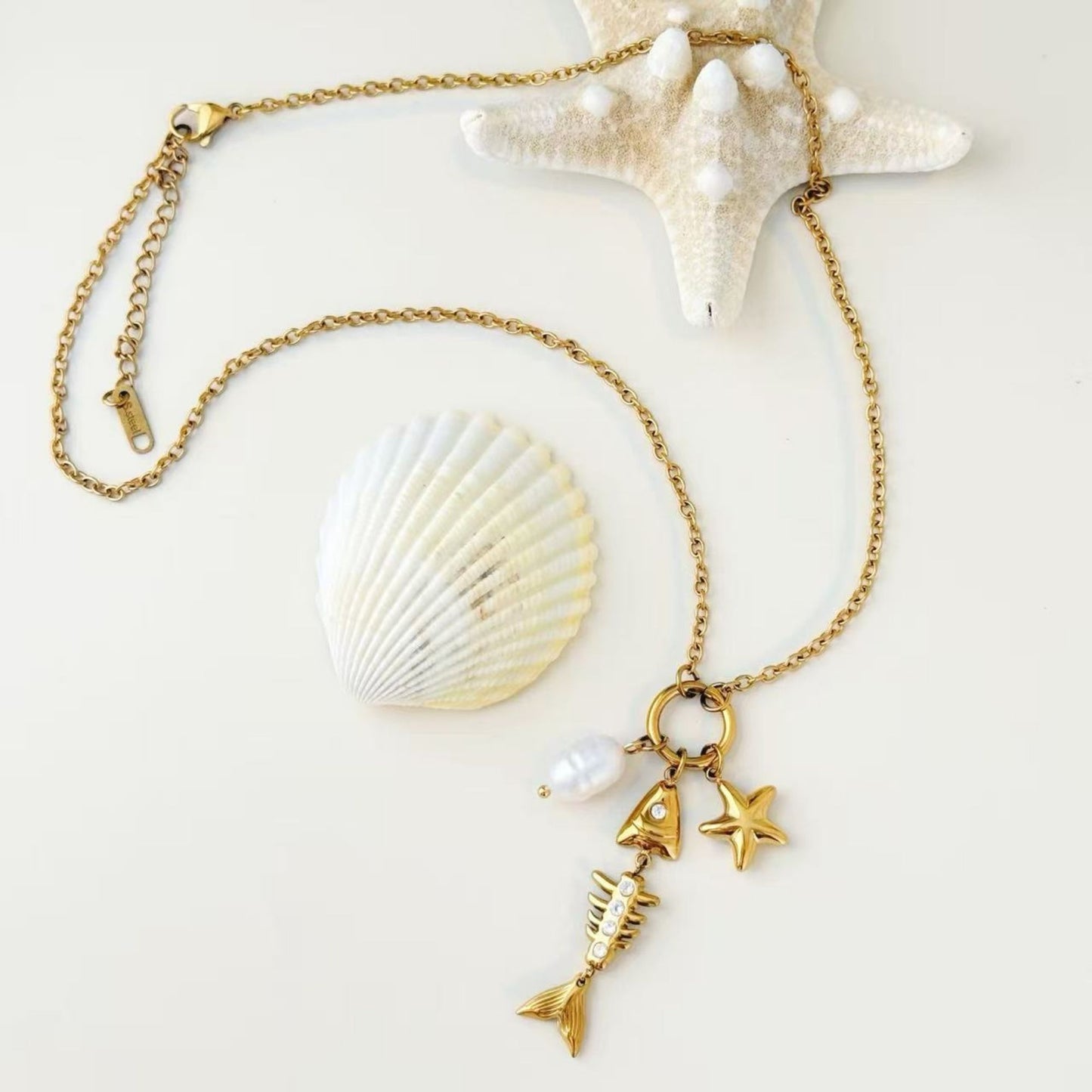 Gold sea charm necklace styled with shells in soft natural light.