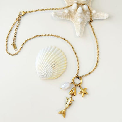 Gold sea charm necklace styled with shells in soft natural light.