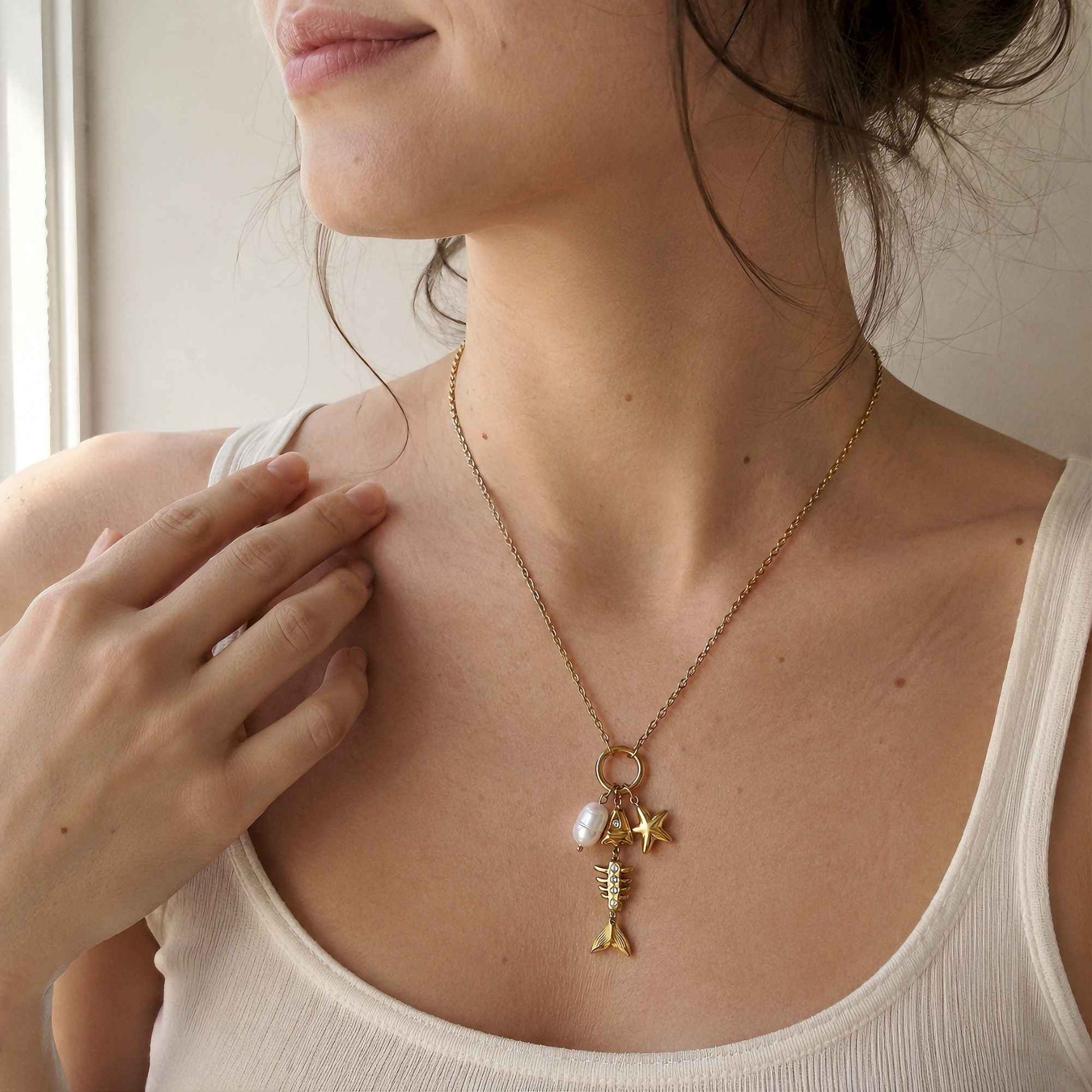 Model wearing a gold sea-inspired charm necklace with a white tank in soft natural light.