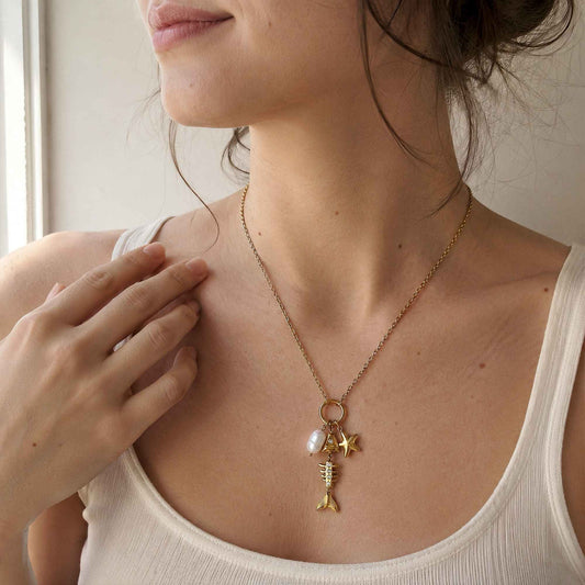 Model wearing a gold sea-inspired charm necklace with a white tank in soft natural light.