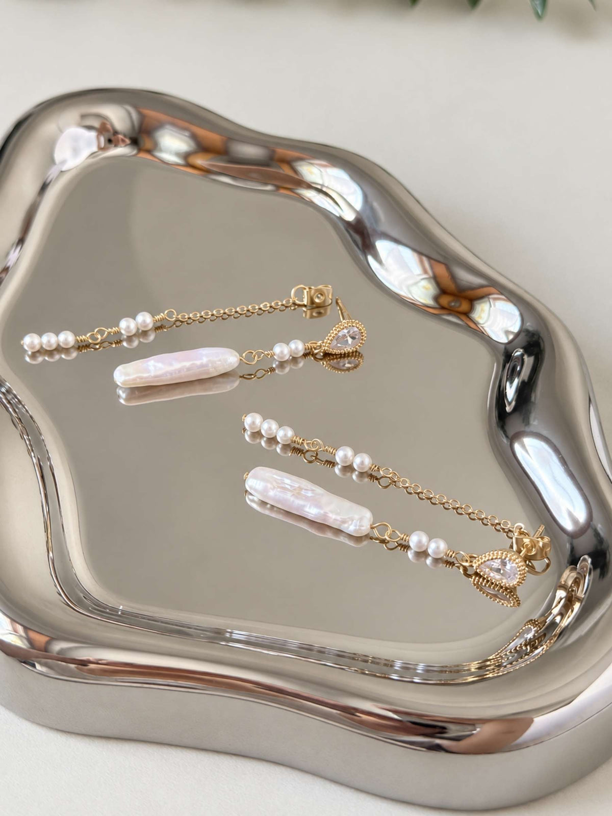 Shift convertible freshwater pearl earrings arranged on a reflective silver tray with long baroque pearl drops.