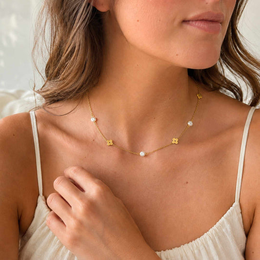 Model wearing a delicate gold flower and freshwater pearl necklace in natural light.