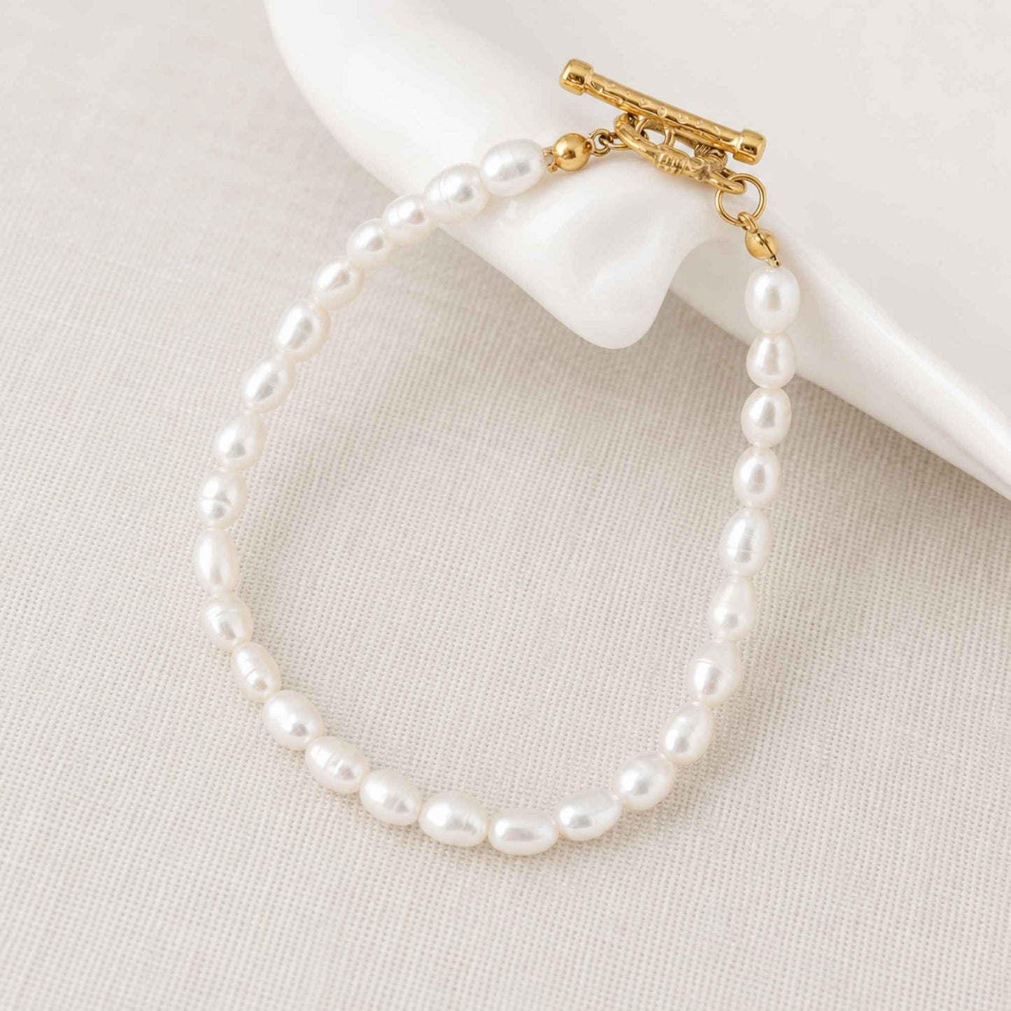Freshwater pearl bracelet placed on soft linen with a gold toggle clasp.