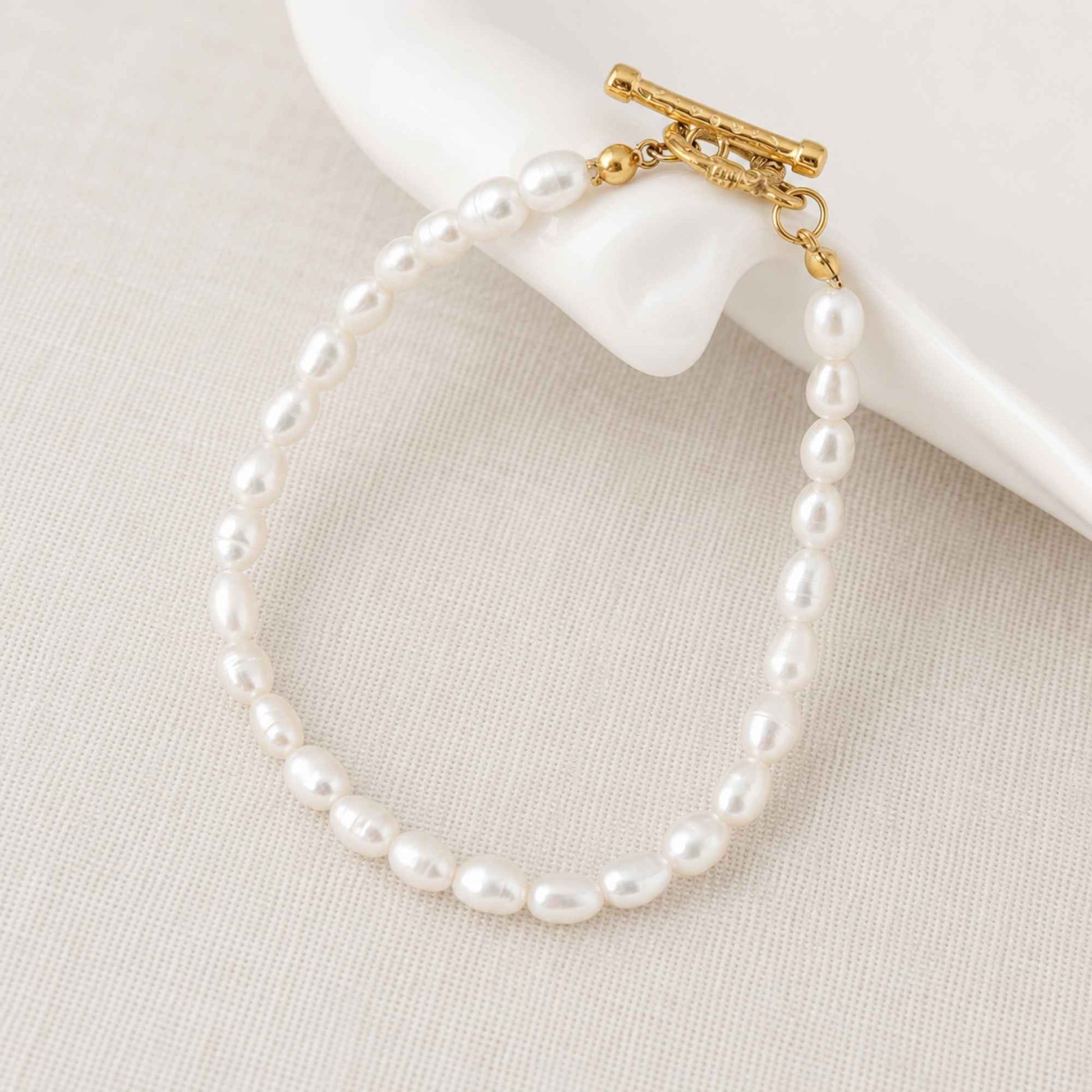 Freshwater pearl bracelet placed on soft linen with a gold toggle clasp.