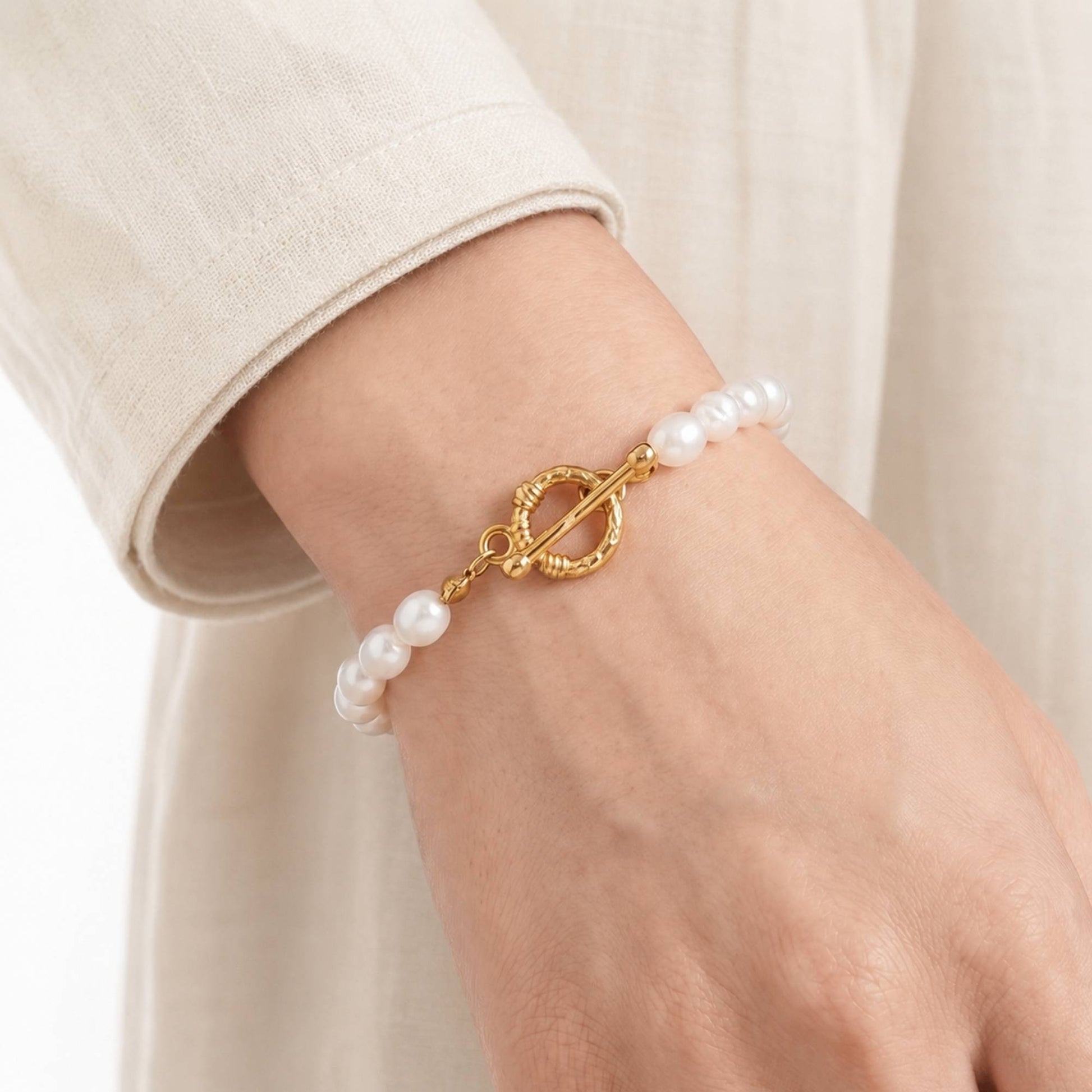 Model wearing a freshwater pearl bracelet with a gold toggle clasp on the wrist.