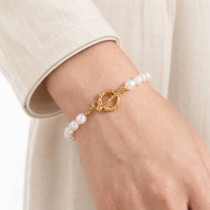 Model wearing a freshwater pearl bracelet with a gold toggle clasp on the wrist.