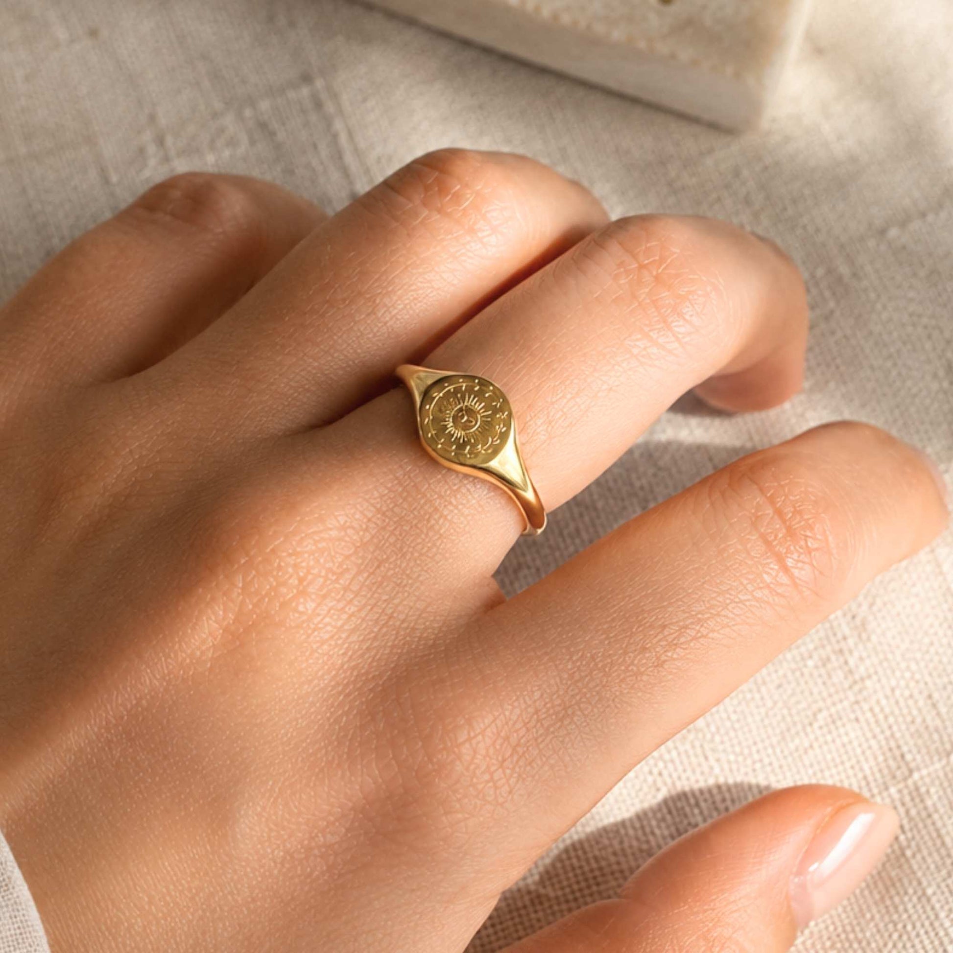 Waterproof gold sun signet ring worn on the hand in warm natural light