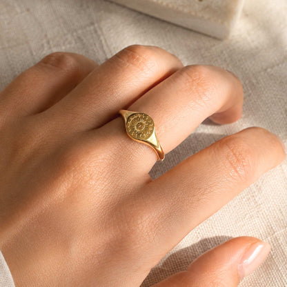 Waterproof gold sun signet ring worn on the hand in warm natural light