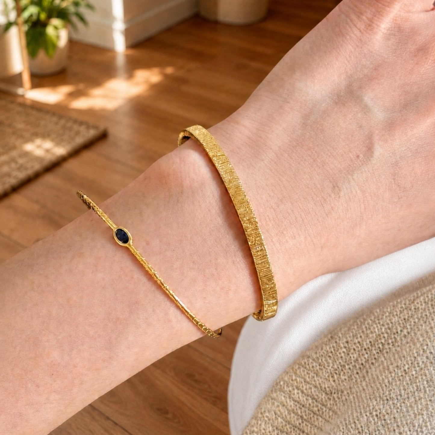 Gold cuff bracelet set with a slim blue stone bracelet worn on the wrist