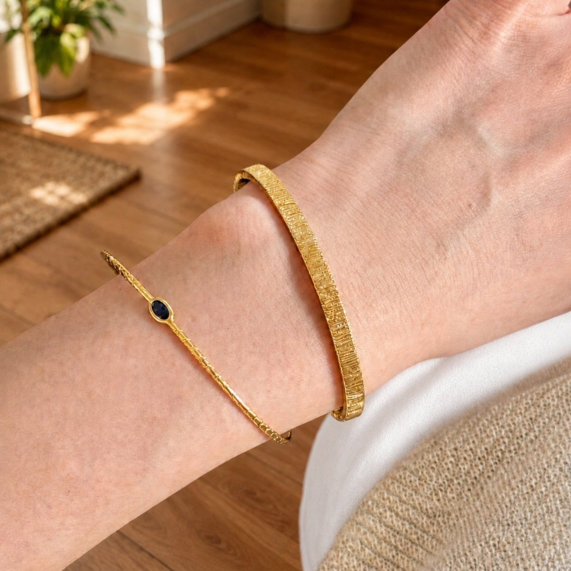 Gold cuff bracelet set with a slim blue stone bracelet worn on the wrist