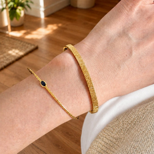 Gold cuff bracelet set with a slim blue stone bracelet worn on the wrist