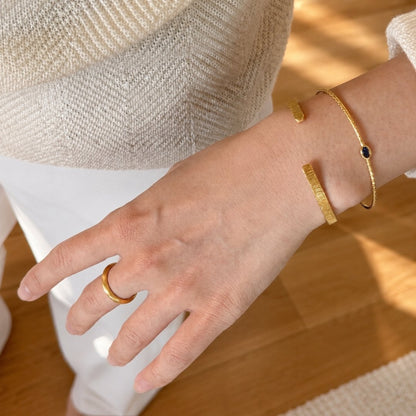 Two gold cuff bracelets stacked with a textured band and blue stone accent