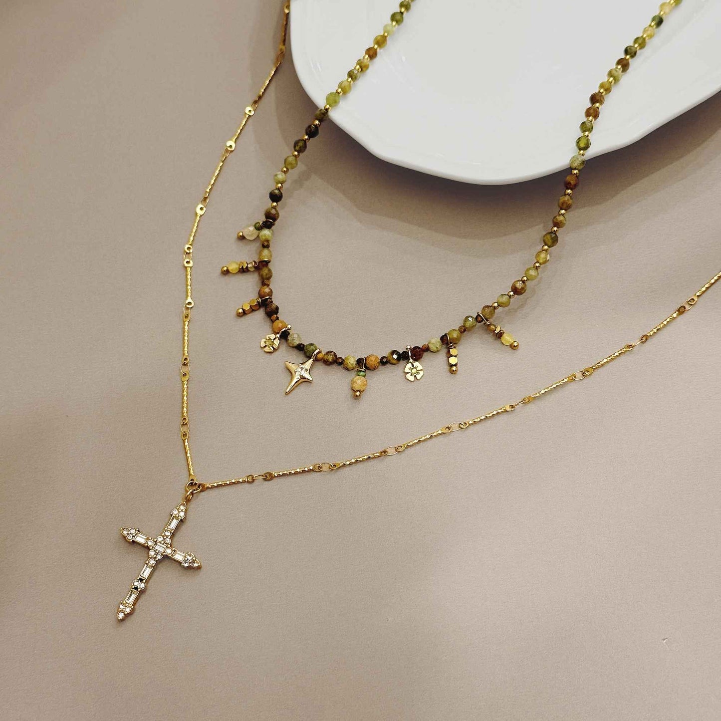 Steadfast necklace set styled flat with natural stone beads and a crystal-detailed gold cross necklace.