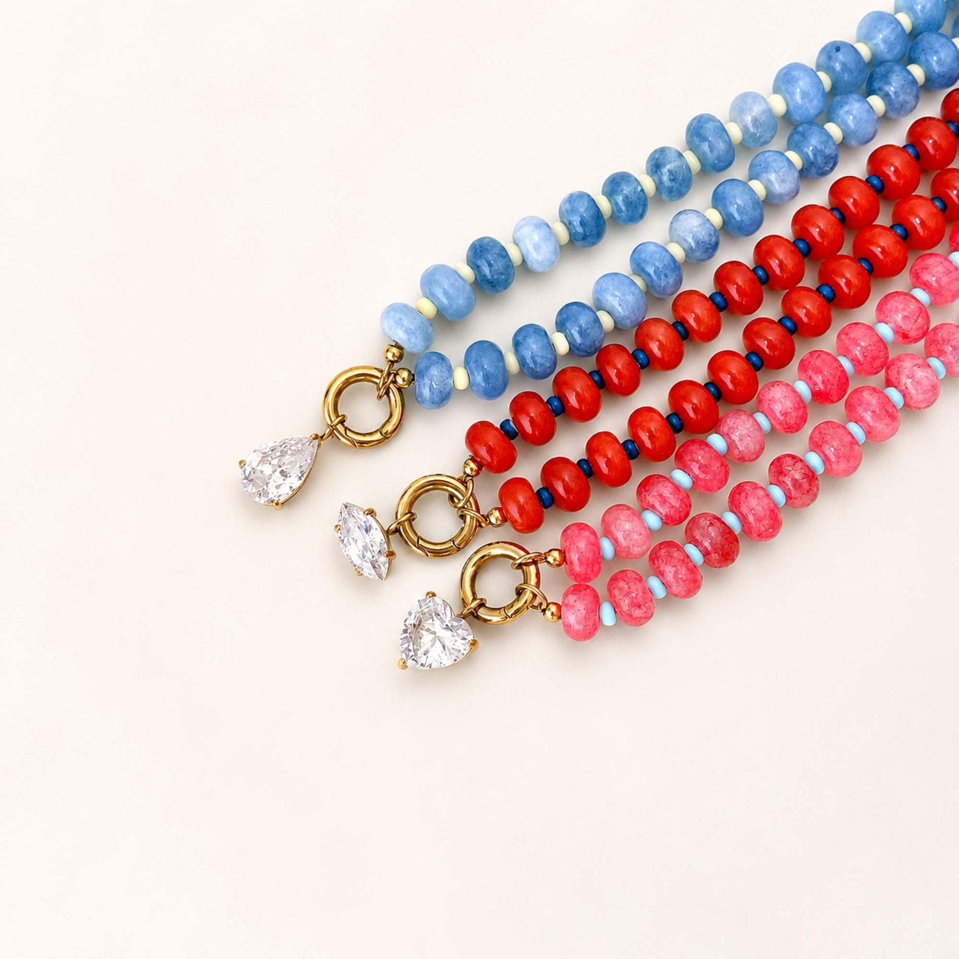 Blue, red, and pink natural stone beaded necklaces arranged together on a soft neutral background.