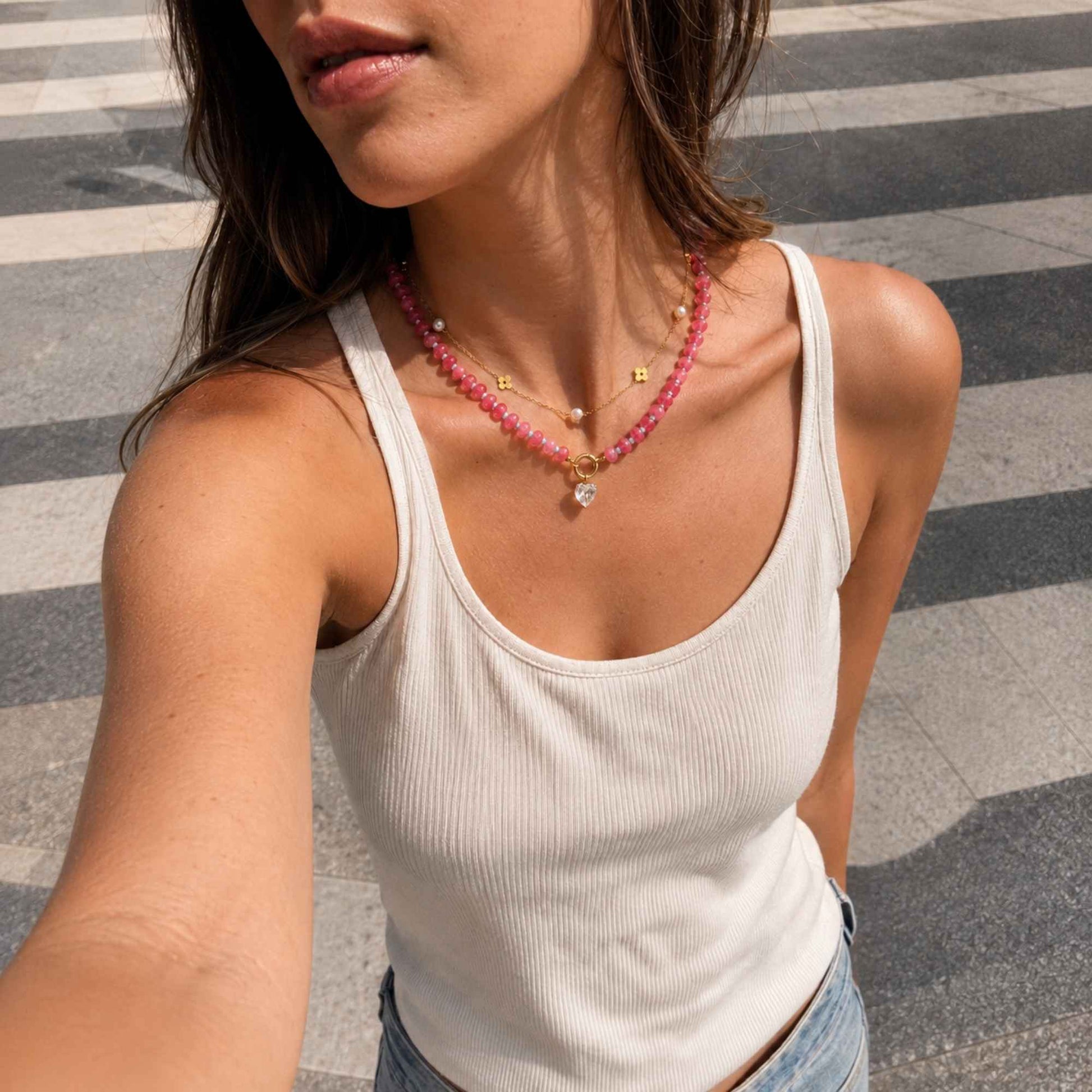 Pink natural stone beaded necklace layered with a delicate pearl chain in natural sunlight.