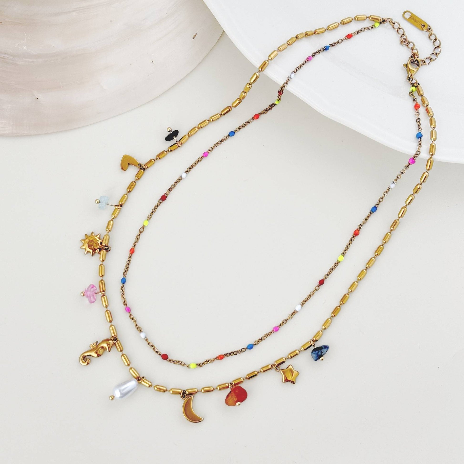 Gold layered charm necklace arranged on a light shell plate with colorful bead details.