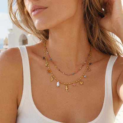 Model wearing a gold layered charm necklace with colorful beads and small summer pendants.