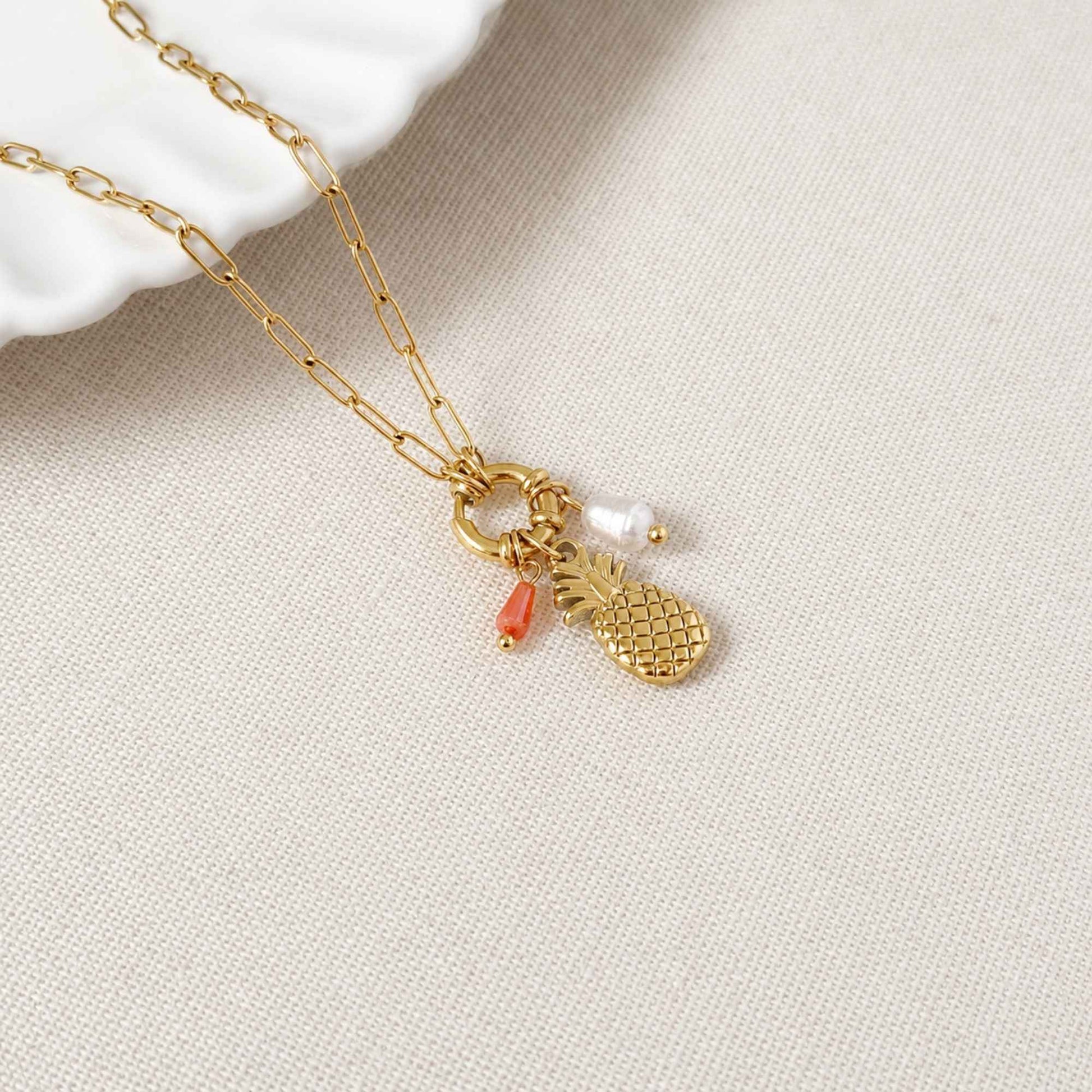 Close-up of pineapple charm, freshwater pearl, orange natural stone accent, and gold chain.