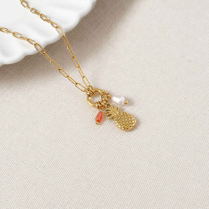 Close-up of pineapple charm, freshwater pearl, orange natural stone accent, and gold chain.